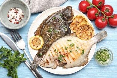 Photo of Tasty roasted flounder fish with herbs and lemon slices served on light blue wooden table, flat lay. Homemade seafood dish