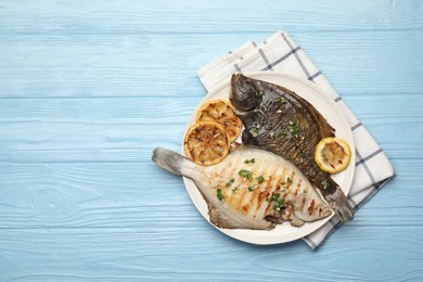 Photo of Homemade seafood dish. Tasty roasted flounder fish with herbs and lemon slices on light blue wooden table, top view. Space for text