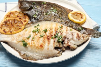 Photo of Tasty roasted flounder fish with herbs and lemon slices on light blue wooden table, closeup. Homemade seafood dish