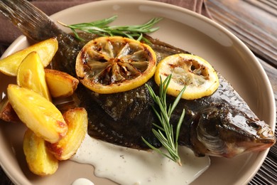 Photo of Tasty roasted flounder fish with rosemary, potato and lemon slices on wooden table, closeup. Homemade seafood dish