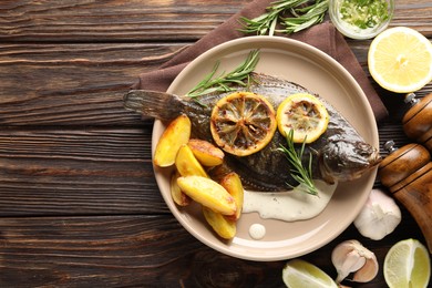 Photo of Homemade seafood dish. Tasty roasted flounder fish with rosemary, potato and lemon slices on wooden table, flat lay. Space for text
