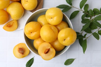 Photo of Ripe yellow cherry plums on white tiled table, flat lay