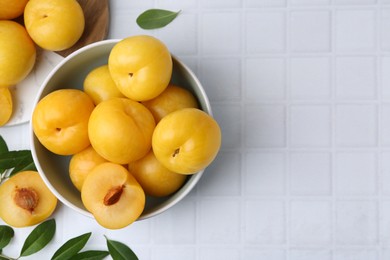 Photo of Ripe yellow cherry plums on white tiled table, flat lay. Space for text