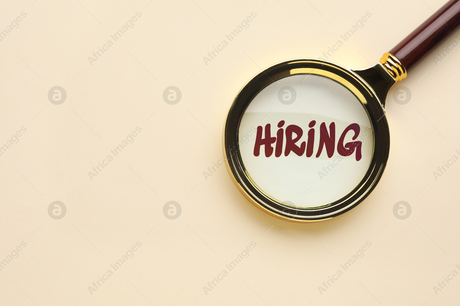 Image of Word Hiring on beige background, view through magnifying glass