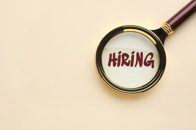 Image of Word Hiring on beige background, view through magnifying glass