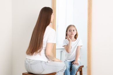 Image of Young woman seeing herself as child in mirror. Conceptual collage about past and future, flow of time, age