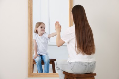 Image of Young woman seeing herself as child in mirror. Conceptual collage about past and future, flow of time, age