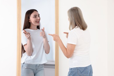 Image of Senior woman seeing herself as young girl in mirror. Conceptual collage about past and future, flow of time, age