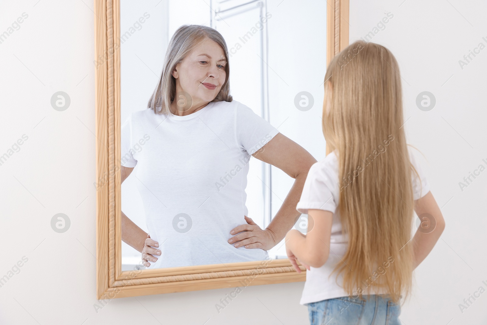 Image of Little girl seeing herself as senior woman in mirror. Conceptual collage about past and future, flow of time, age