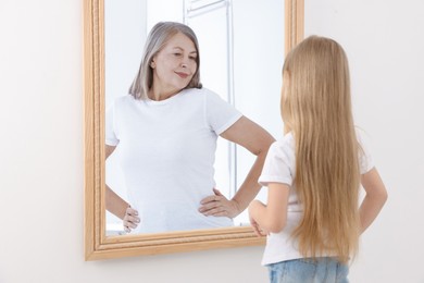 Image of Little girl seeing herself as senior woman in mirror. Conceptual collage about past and future, flow of time, age