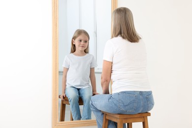 Image of Senior woman seeing herself as child in mirror. Conceptual collage about past and future, flow of time, age