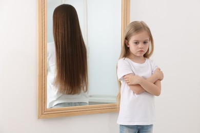 Image of Sad little girl in room. Young woman as reflection in mirror. Conceptual collage about past and future, flow of time, age