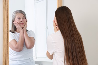 Image of Young girl seeing herself as senior woman in mirror. Conceptual collage about past and future, flow of time, age
