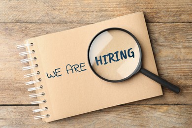 Image of We are hiring. Notebook with inscription and magnifying glass on wooden table, top view