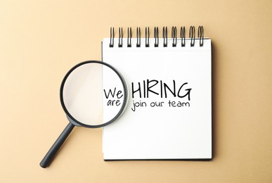 Image of We are hiring, join our team. Notebook with inscription and magnifying glass on beige background, top view