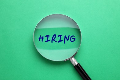 Image of Word Hiring on green background, view through magnifying glass