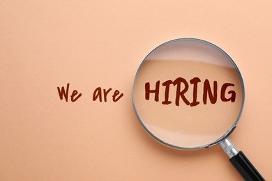 Image of We are hiring. Inscription and magnifying glass on beige pink background, top view
