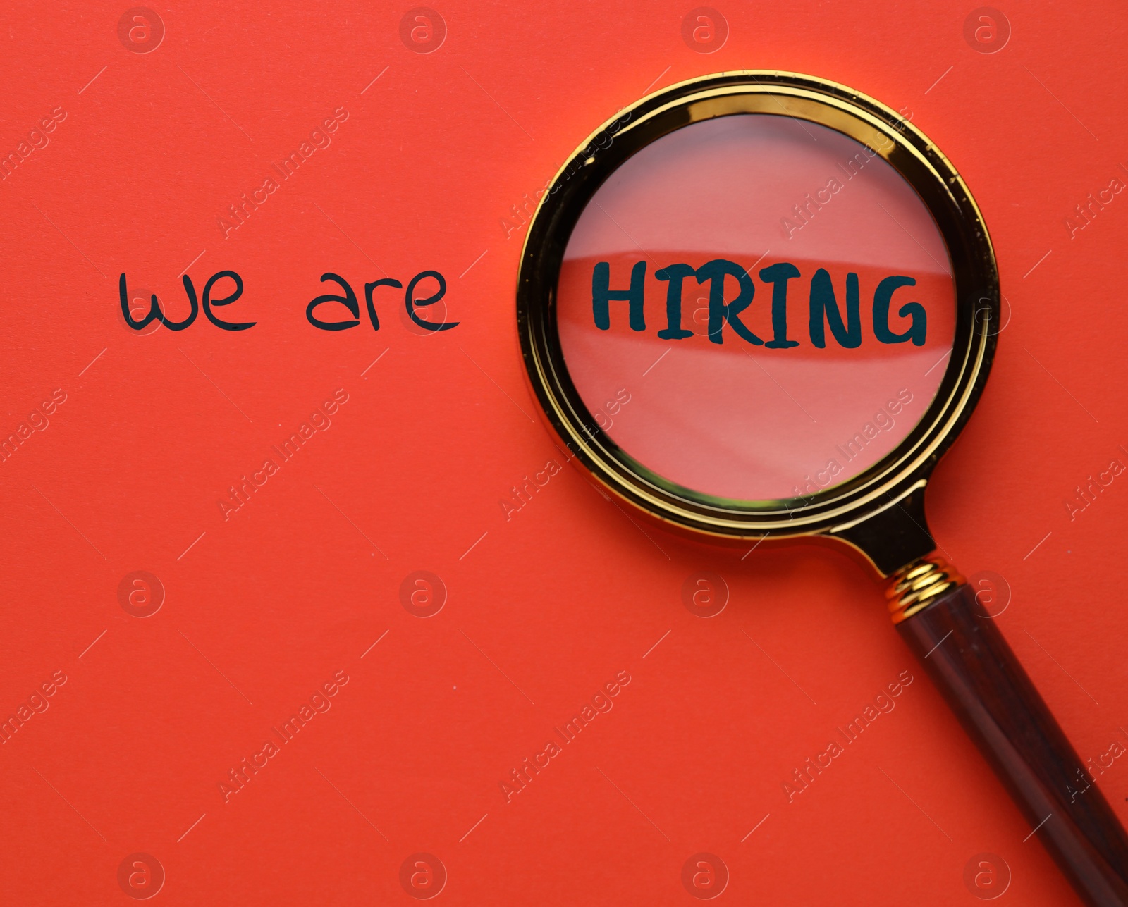Image of We are hiring. Inscription and magnifying glass on red background, top view
