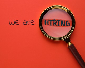 Image of We are hiring. Inscription and magnifying glass on red background, top view
