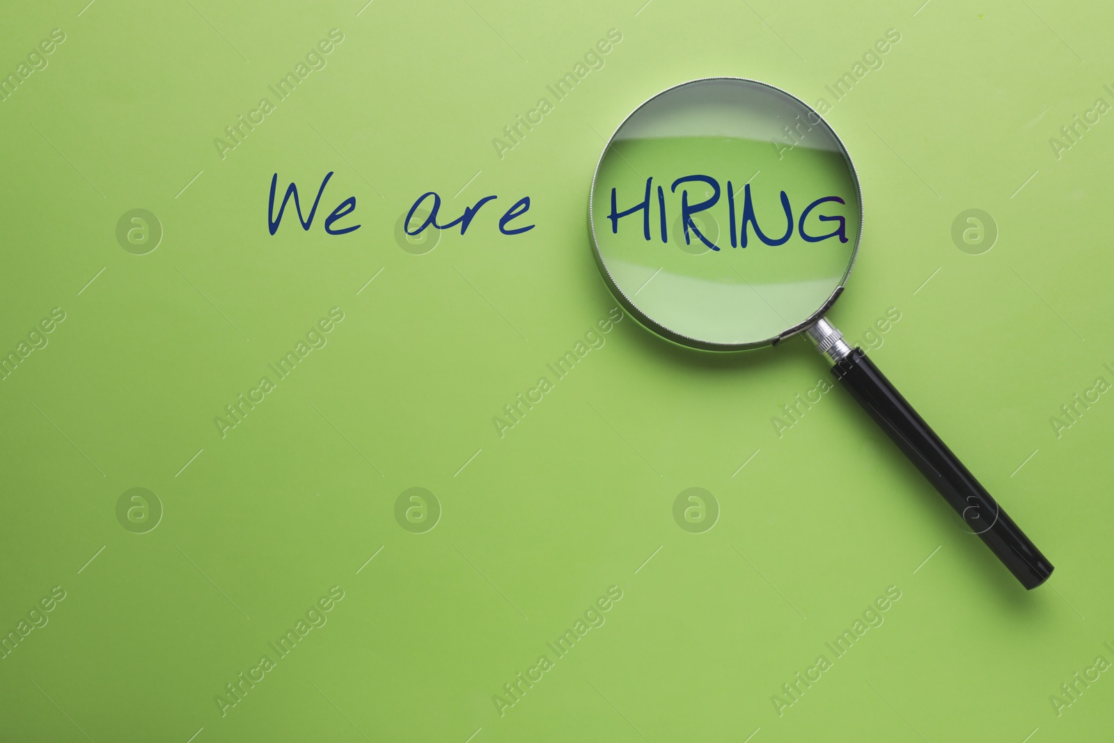 Image of We are hiring. Inscription and magnifying glass on green background, top view