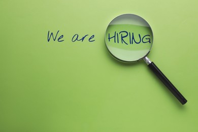 Image of We are hiring. Inscription and magnifying glass on green background, top view
