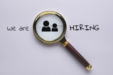 Image of We are hiring. Magnifying glass with human icon and inscription on grey background, top view