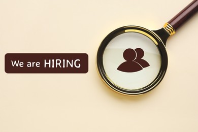 Image of We are hiring. Magnifying glass with human icon and inscription on beige background, top view