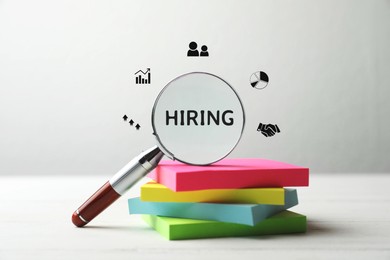 Image of We are hiring, join our team. Magnifying glass with word inside and note papers on white table