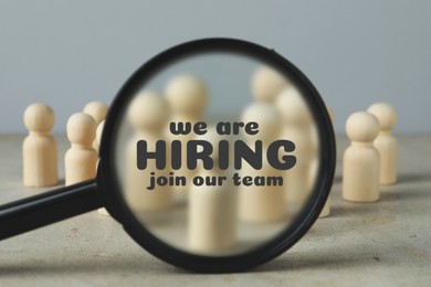 Image of We are hiring, join our team. Magnifying glass with inscription inside against human figures on grey table