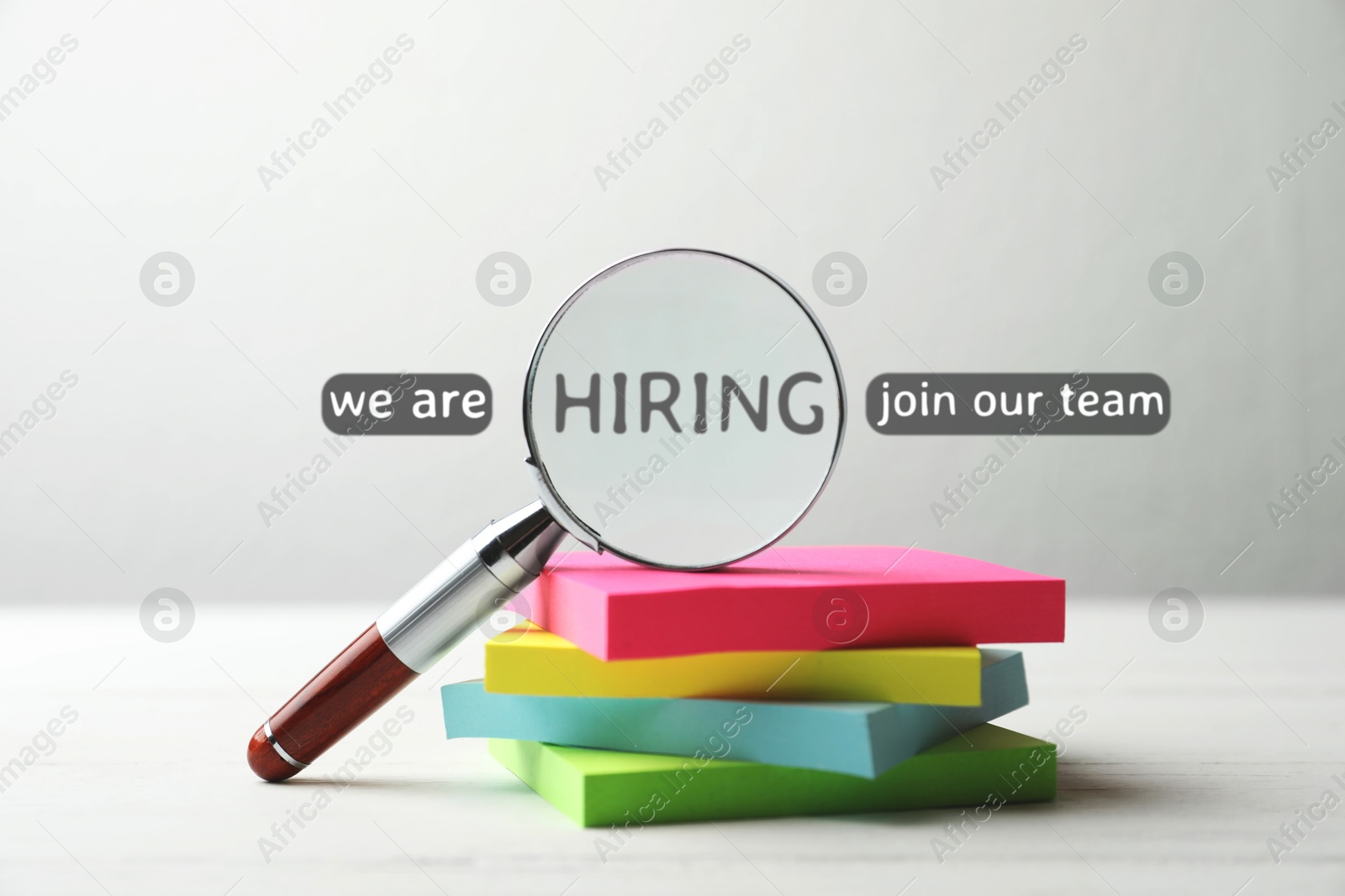 Image of We are hiring, join our team. Magnifying glass with word inside and note paper on white table