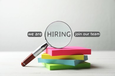 Image of We are hiring, join our team. Magnifying glass with word inside and note paper on white table