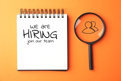 Image of We are hiring, join our team. Notebook with inscription and magnifying glass on orange background, top view