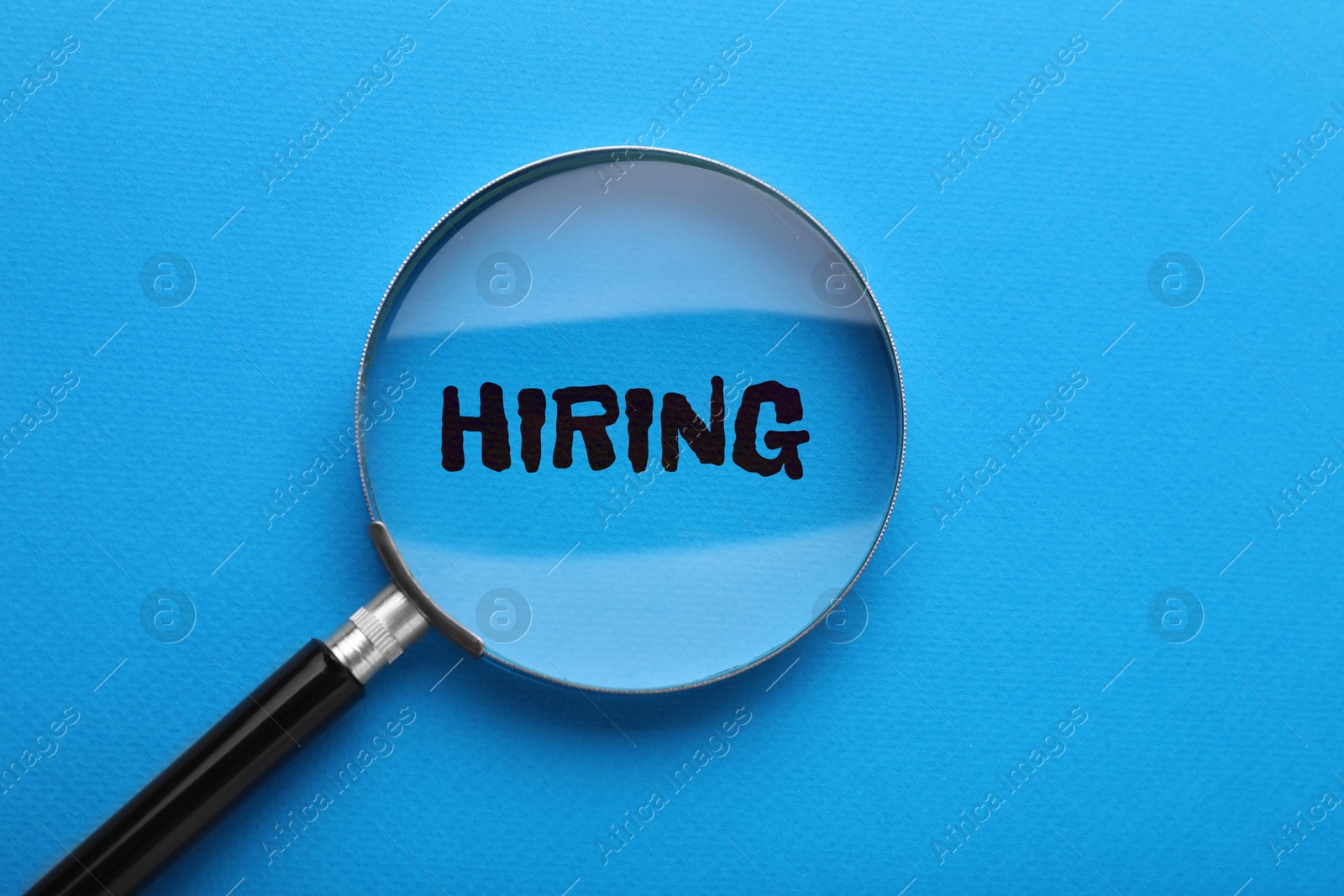 Image of Word Hiring on blue background, view through magnifying glass