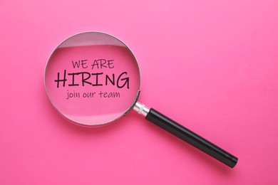 Image of We are hiring, join our team. Inscription and magnifying glass on pink background, top view