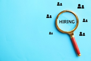 Image of Word Hiring and human icons on light blue background, view through magnifying glass