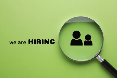 Image of We are hiring. Magnifying glass with human icon and inscription on green background, top view