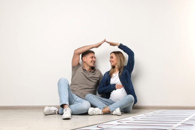 Image of Pregnant woman and her husband on warm floor at home, double exposure with underfloor heating system