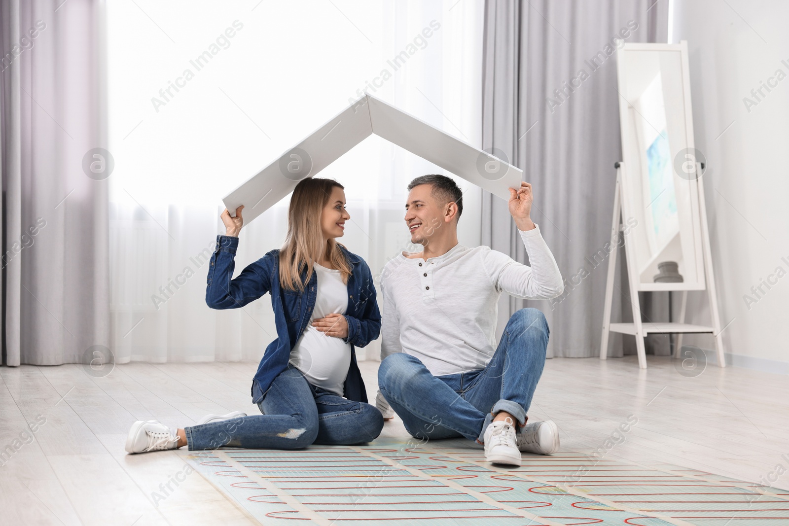 Image of Pregnant woman and her husband on warm floor at home, double exposure with underfloor heating system