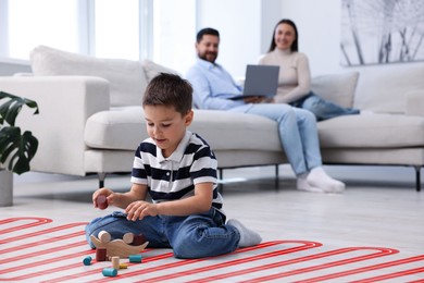Image of Boy playing on warm floor and his parents on sofa at home, double exposure with underfloor heating system