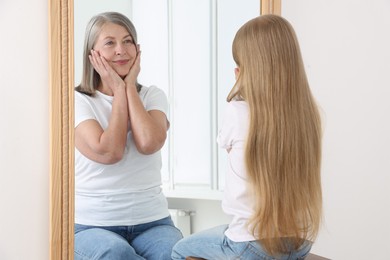 Image of Little girl seeing herself as senior woman in mirror. Conceptual collage about past and future, flow of time, age