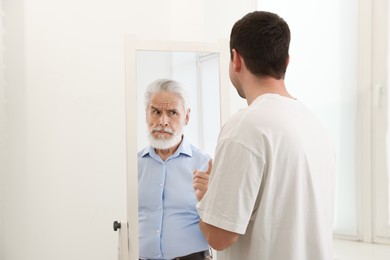 Image of Man seeing himself as elder in mirror. Conceptual collage about past and future, flow of time, age