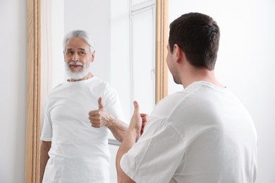 Image of Man seeing himself as elder in mirror. Conceptual collage about past and future, flow of time, age