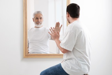 Image of Man seeing himself as elder in mirror. Conceptual collage about past and future, flow of time, age