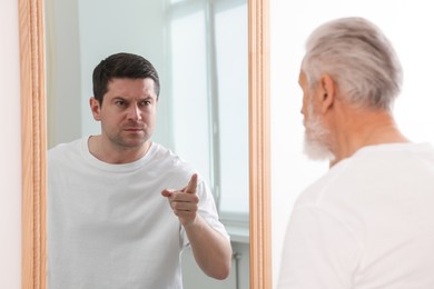 Image of Senior man seeing himself younger in mirror. Conceptual collage about past and future, flow of time, age