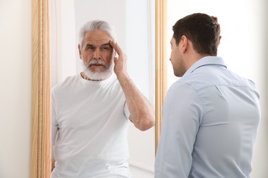 Image of Man seeing himself as elder in mirror. Conceptual collage about past and future, flow of time, age