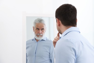 Image of Man seeing himself as elder in mirror. Conceptual collage about past and future, flow of time, age