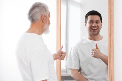 Image of Senior man seeing himself younger in mirror. Conceptual collage about past and future, flow of time, age