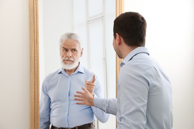 Image of Man seeing himself as elder in mirror. Conceptual collage about past and future, flow of time, age