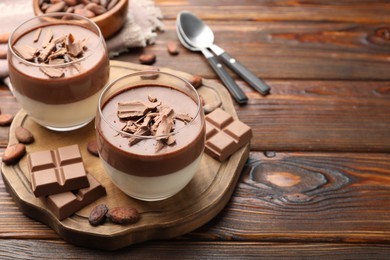 Photo of Delicious panna cotta in glasses, cocoa beans and chocolate pieces on wooden table. Space for text