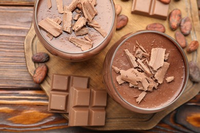Photo of Delicious chocolate panna cotta in glasses, cocoa beans and chocolate pieces on wooden table, flat lay